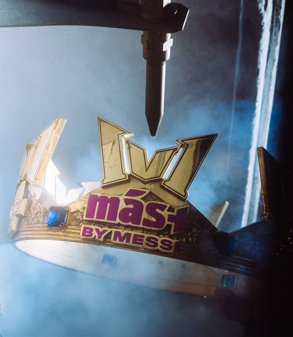 A golden crown with M&aacute;s by Messi logo